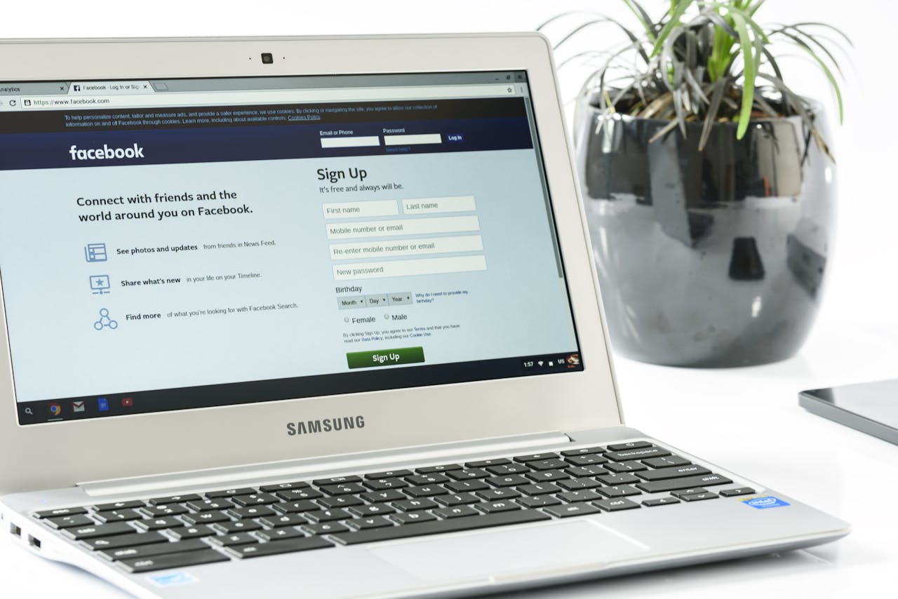 services-04 Open Samsung laptop showing Facebook sign-up page next to a potted plant. Ideal for technology themes.