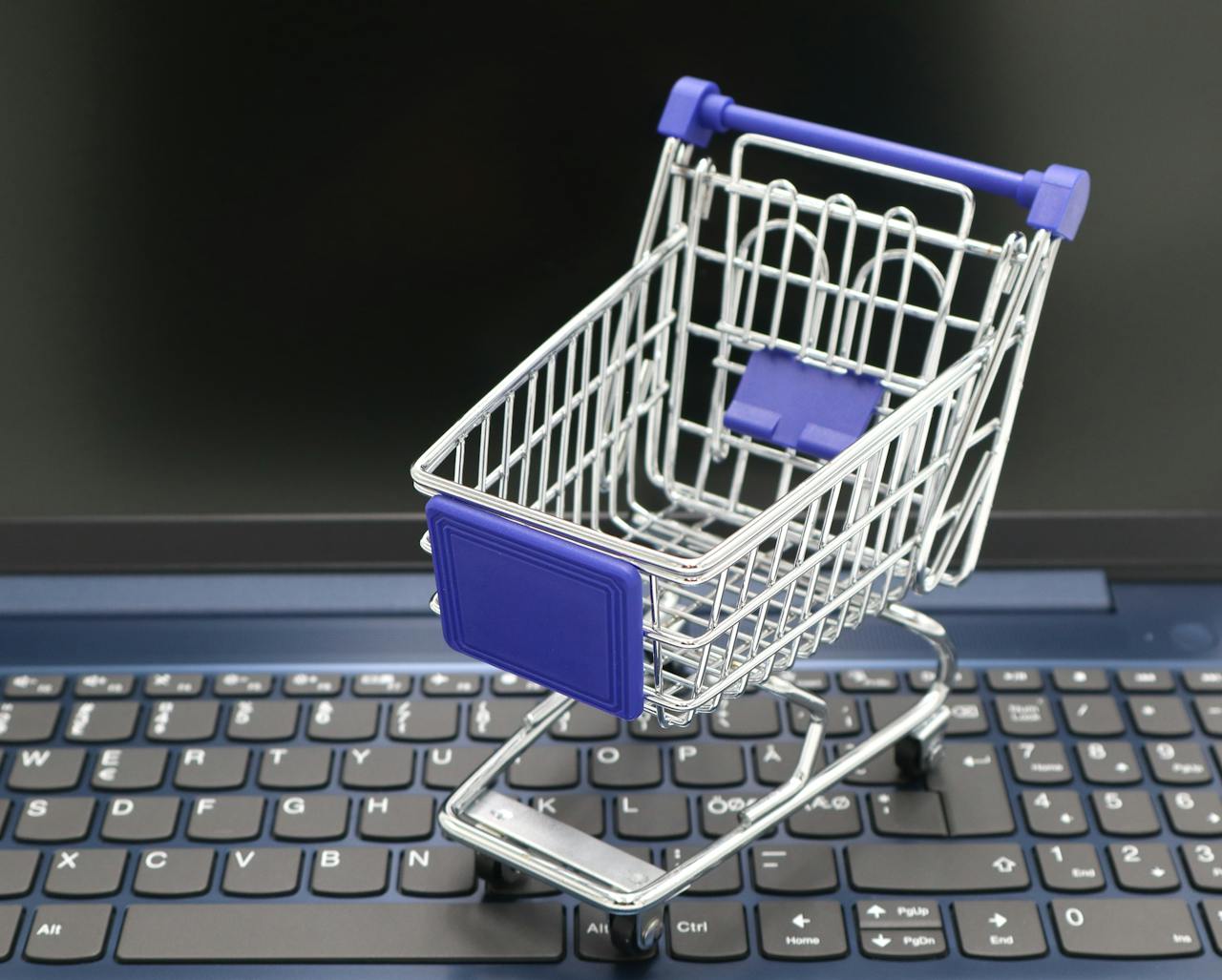 services-03 A mini shopping cart placed on a laptop keyboard, symbolizing online shopping and digital retail.